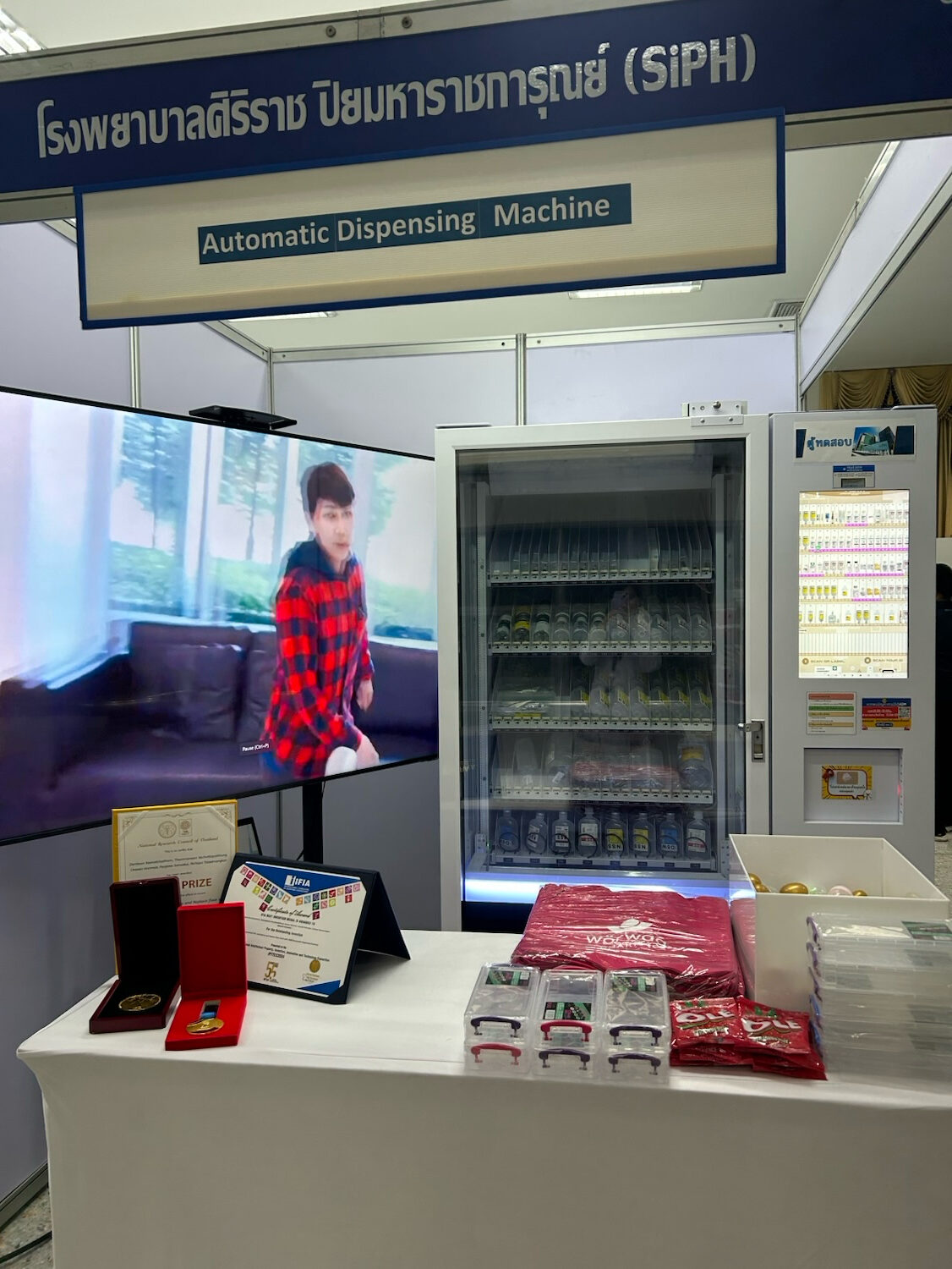 Automatic medicine dispensing machine displayed at a healthcare exhibition in Thailand, with awards and certificates