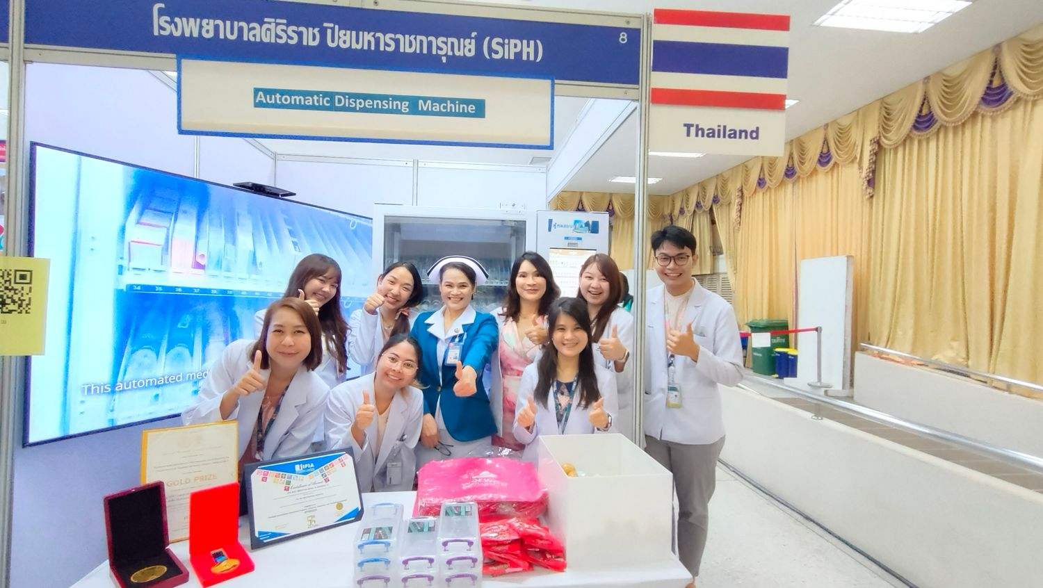 Medical professionals from Siriraj Piyamaharajgarun Hospital posing with an automatic dispensing machine at a healthcare exhibition in Thailand