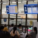 Patients queuing at OPD pharmacy dispensing windows with HAPYopd screens and Robot Pharmacist automated system visible behind glass at Sakaeo Crown Prince Hospital
