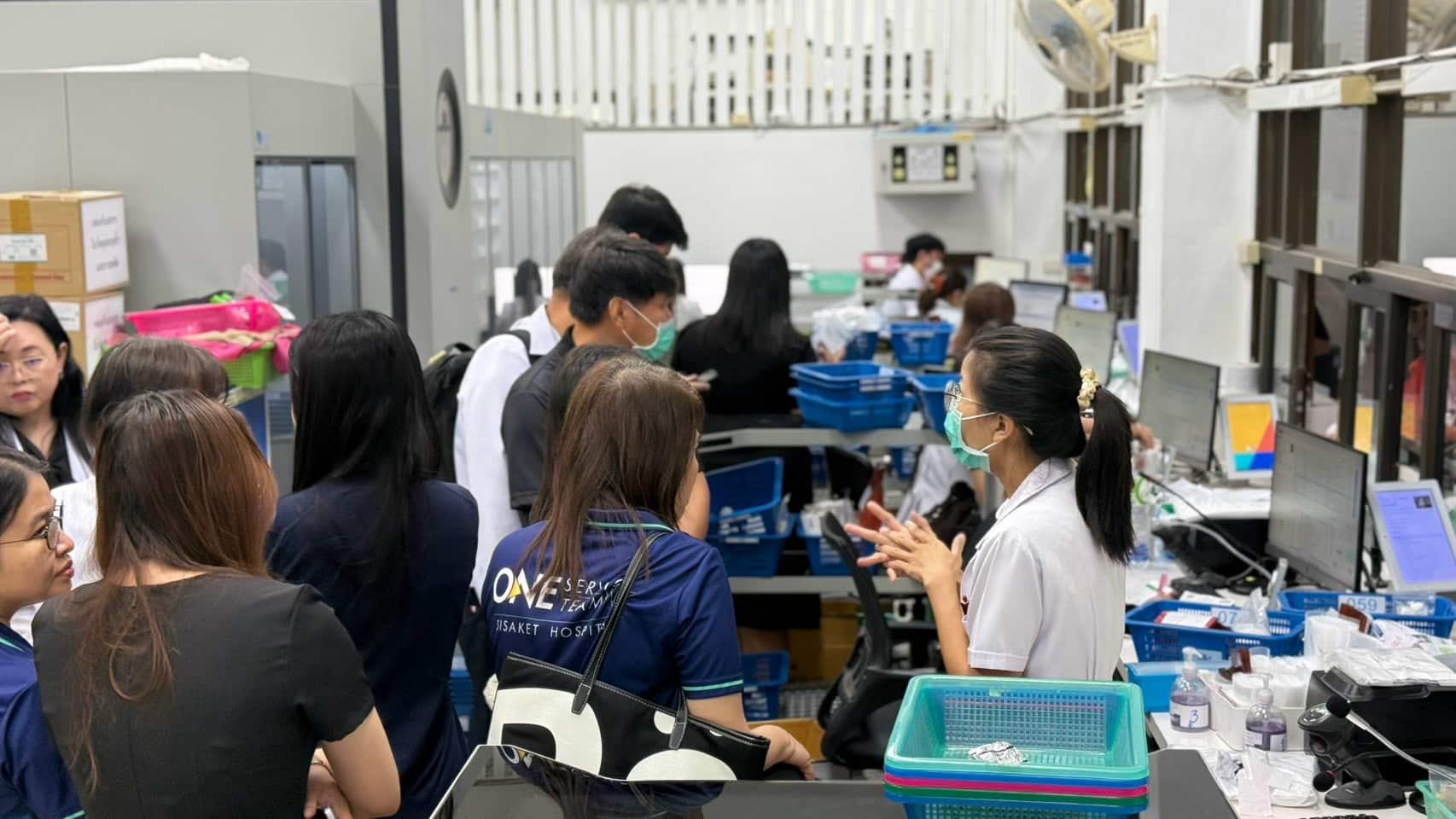 คณะดูงานจากโรงพยาบาลศรีสะเกษ สวมเสื้อ ONE SERVICE TEAM สังเกตกระบวนการจ่ายยาผู้ป่วยนอกจริงที่เคาน์เตอร์ห้องยา รพร.สระแก้ว